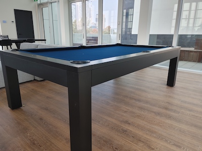 Pool table with a dark blue felt in a room with plenty of windows and natural light.