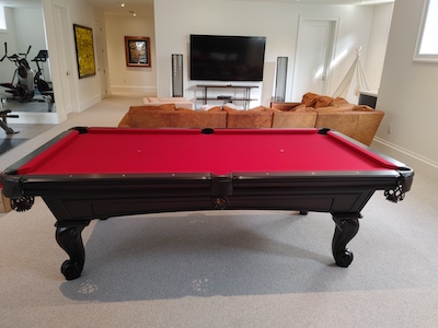 A red felt pool table in a room with a sofa, tv and exercise equipment.