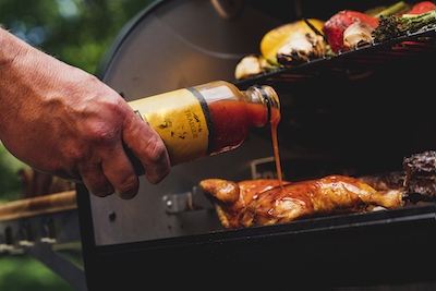 Man adding Traeger's apricot sauce to chicken that is cooking on a wood pellet grill.