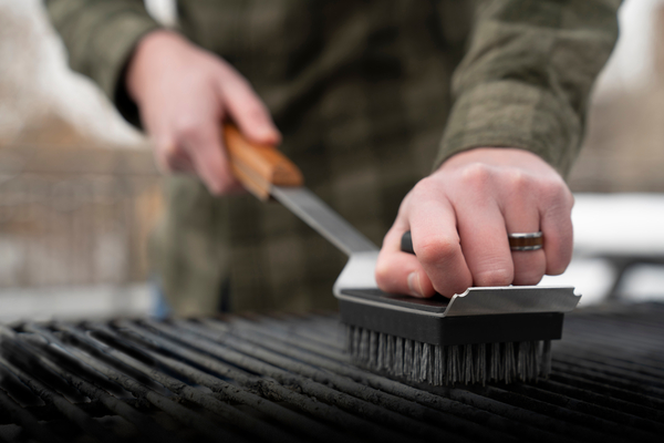 A person in a green shirt scrubbing their Traeger grill with a brush.