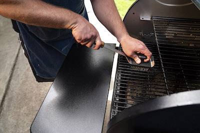 Man using a BBQ cleaning brush on grill grates.