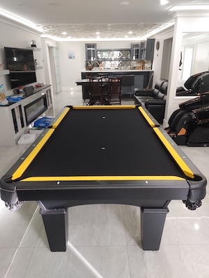 A pool table on a marble floor with a bunch of other sources of entertainment surrounding it, including a TV and kitchen area.