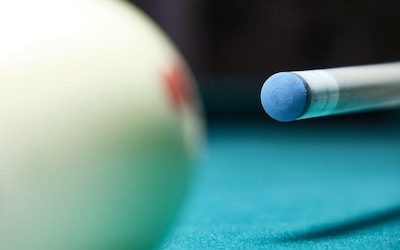 A pool cue with a blue tip aimed at a white cue ball on a blue felt pool table.