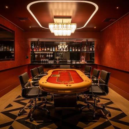 Casino-style poker table with black chairs in a red private game room with a bar.