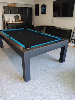 A black and blue pool table on a cement floor in a room with a TV on the wall.