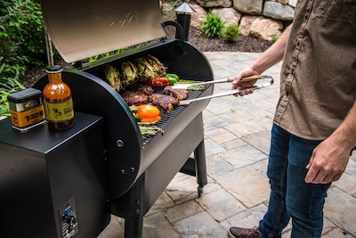 A person with tongs flipping over food in an open barbeque outside.