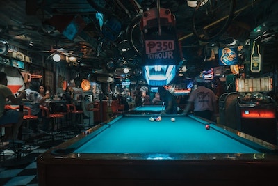 A green felt pool table in a bar with neon lights on the walls.