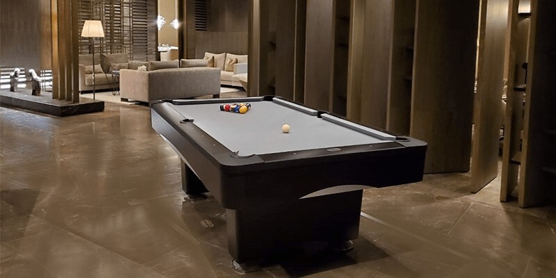 Luxury game room featuring a modern black pool table with gray felt, polished floors, and upscale lounge seating