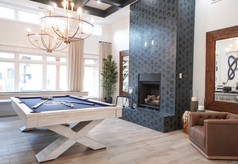 Modern game room with pool table, blue tiled fireplace, large windows, and contemporary chandelier lighting