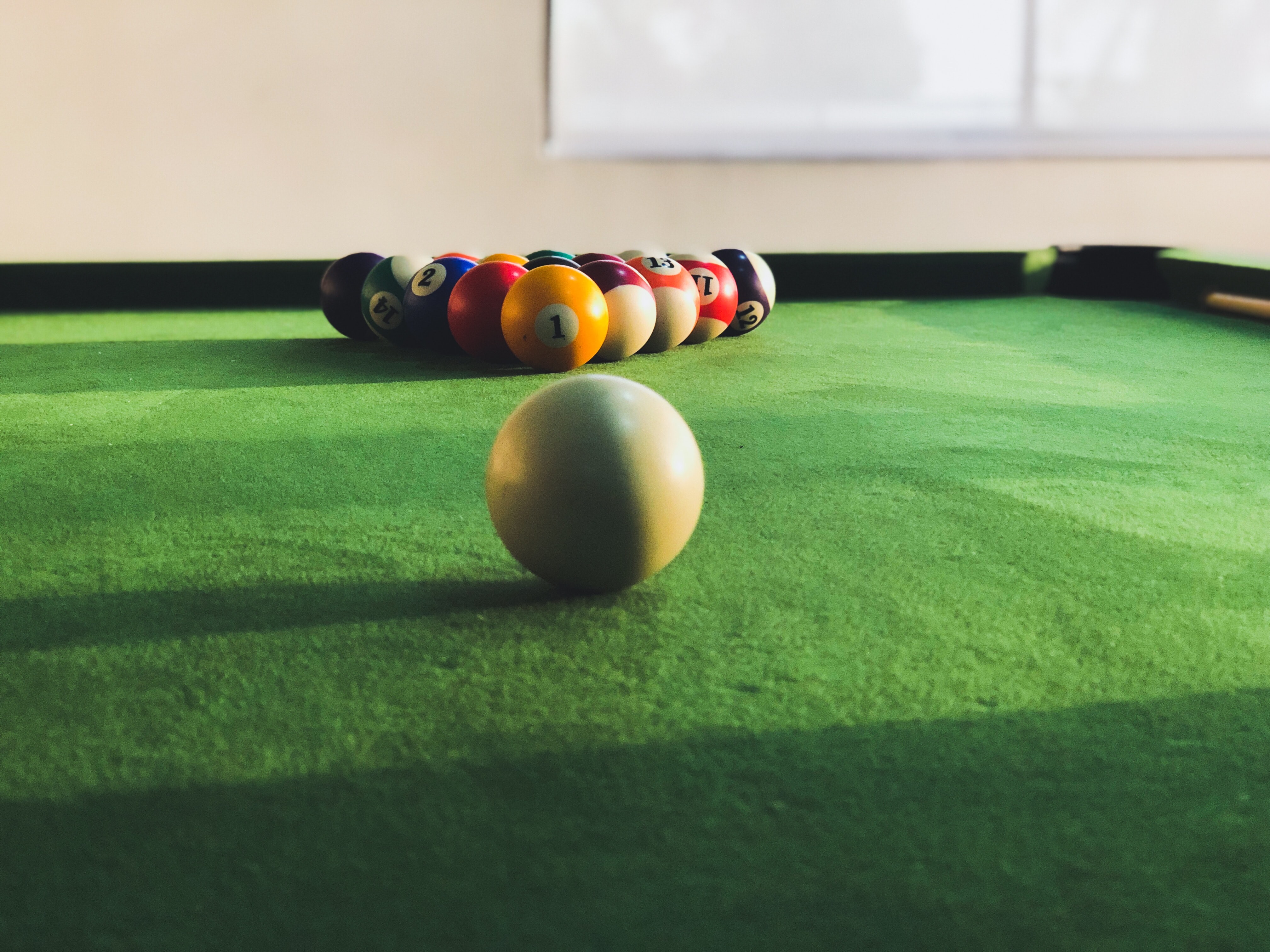white cue ball in front of racked pool balls on a green felt cloth.