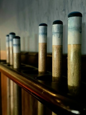 Close-up of pool cue tips lined up on wooden rack against wall in dim lighting.