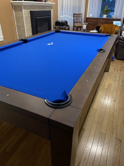 Blue felt pool table on hardwood floors with a seating area in the background.