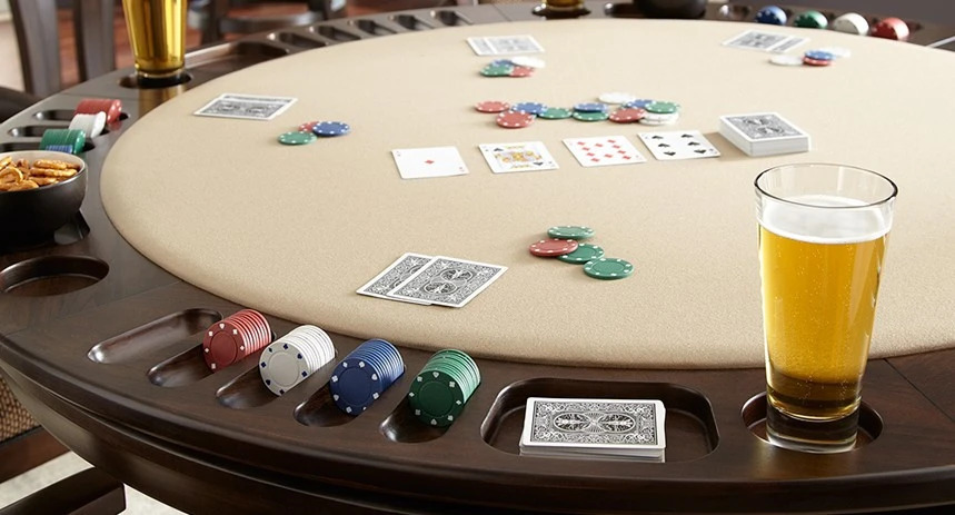 Poker table with playing cards, colorful chips, cup holders, and a glass of beer.