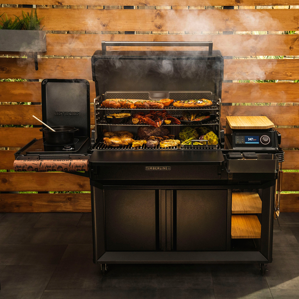 Traeger Timberline XL with open grill and food cooking. Wood panneled fence in the background.