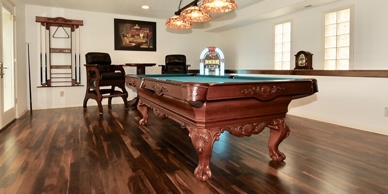 Traditional game room with carved wood pool table, green felt, hardwood floors, cue rack, and classic bar seating