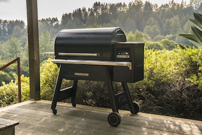 Traeger Timberline 1300 on a wooden patio with lush forest and greenery in the background.